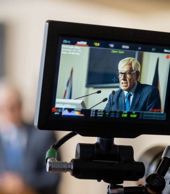 Display of camera with aged male delegate making report at conference Certified Legal Video Services